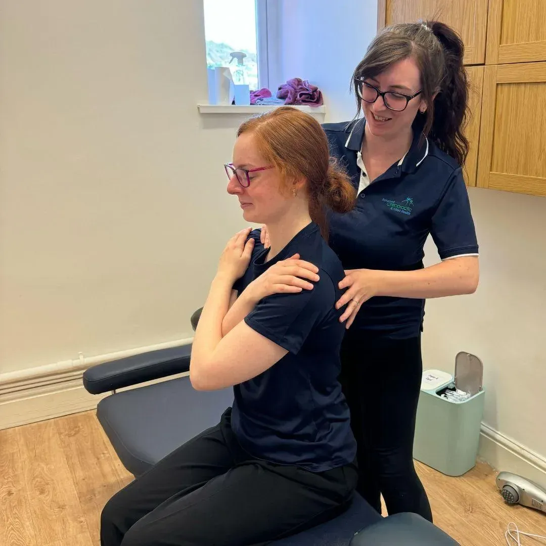 Practitioner assessing a seated patient's shoulder movement in the clinic