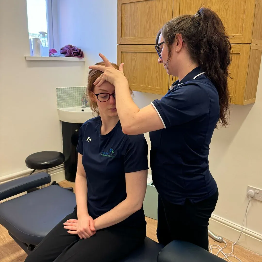 Practitioner examining a seated patient's neck movement in a Bargoed treatment room
